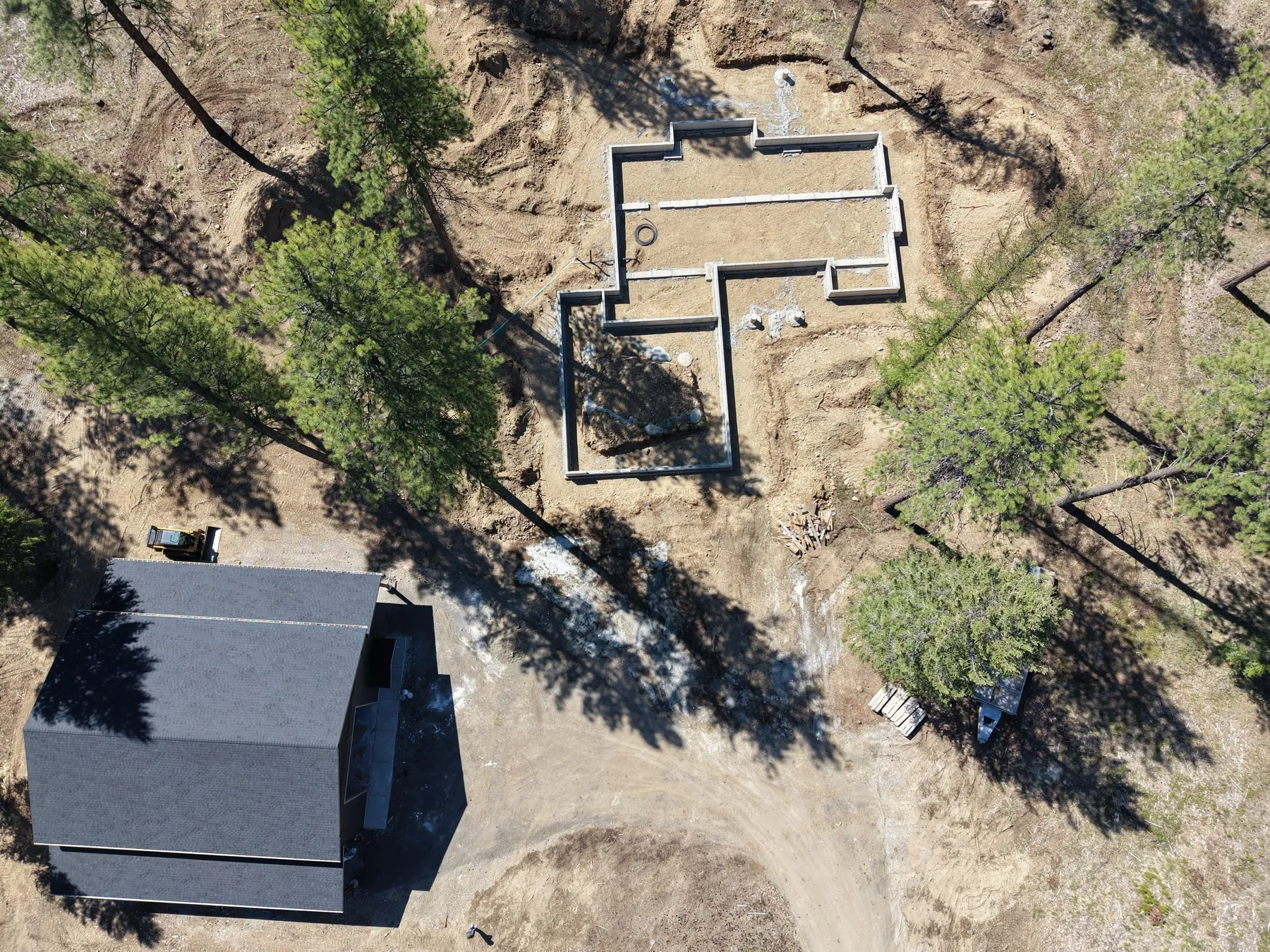 Overhead drone view of the new foundation forms beside the existing shop on the wooded lot.