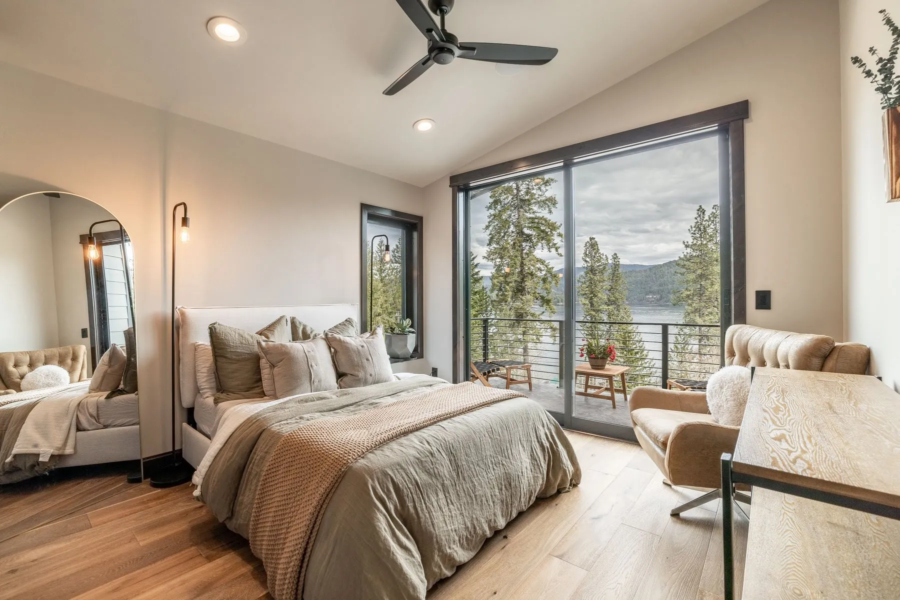 Bright bedroom with a sliding glass door onto a lake-view deck, an upholstered chair and a ceiling fan.