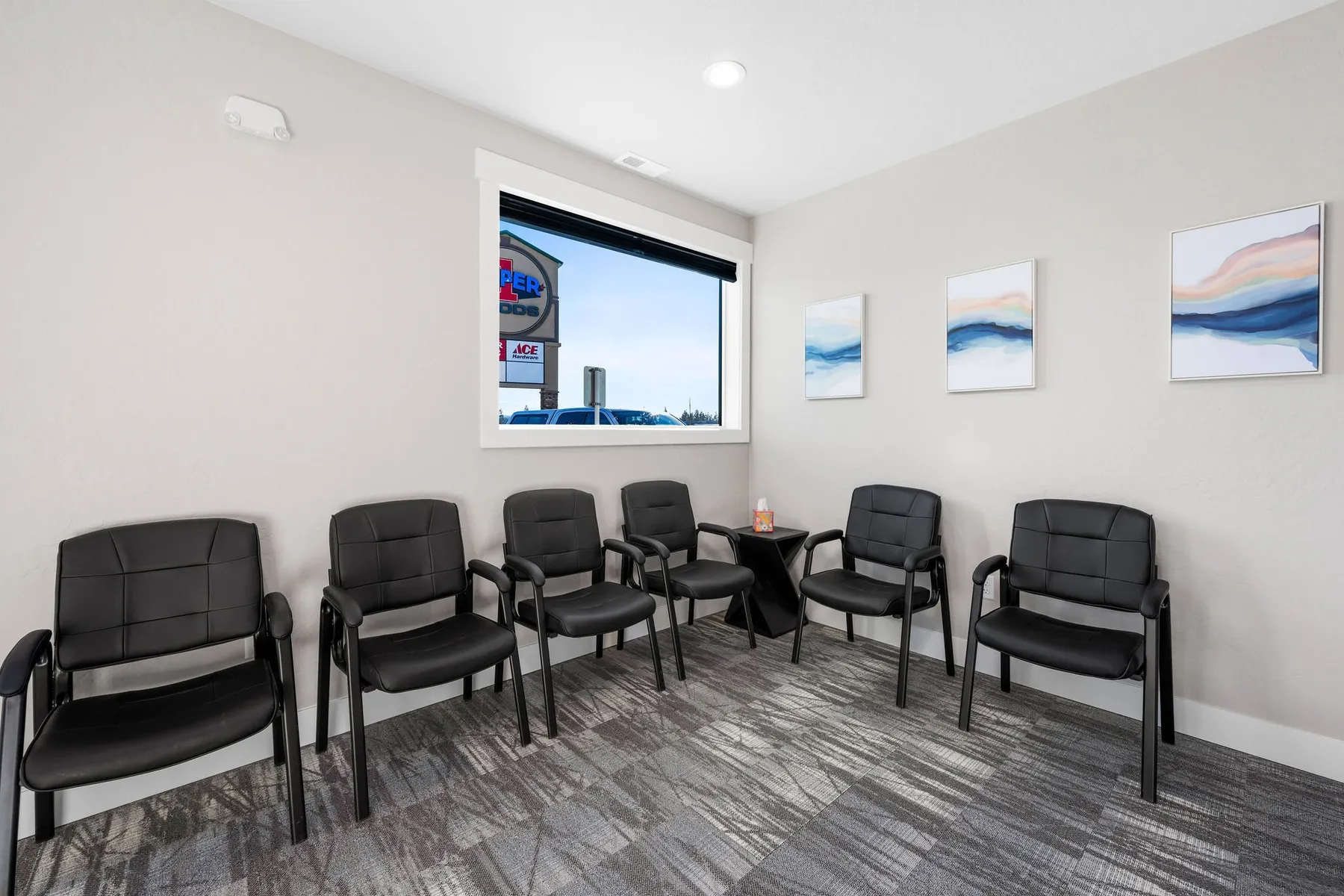 Waiting area with black leather chairs along two walls, framed abstract art and a window to the street.