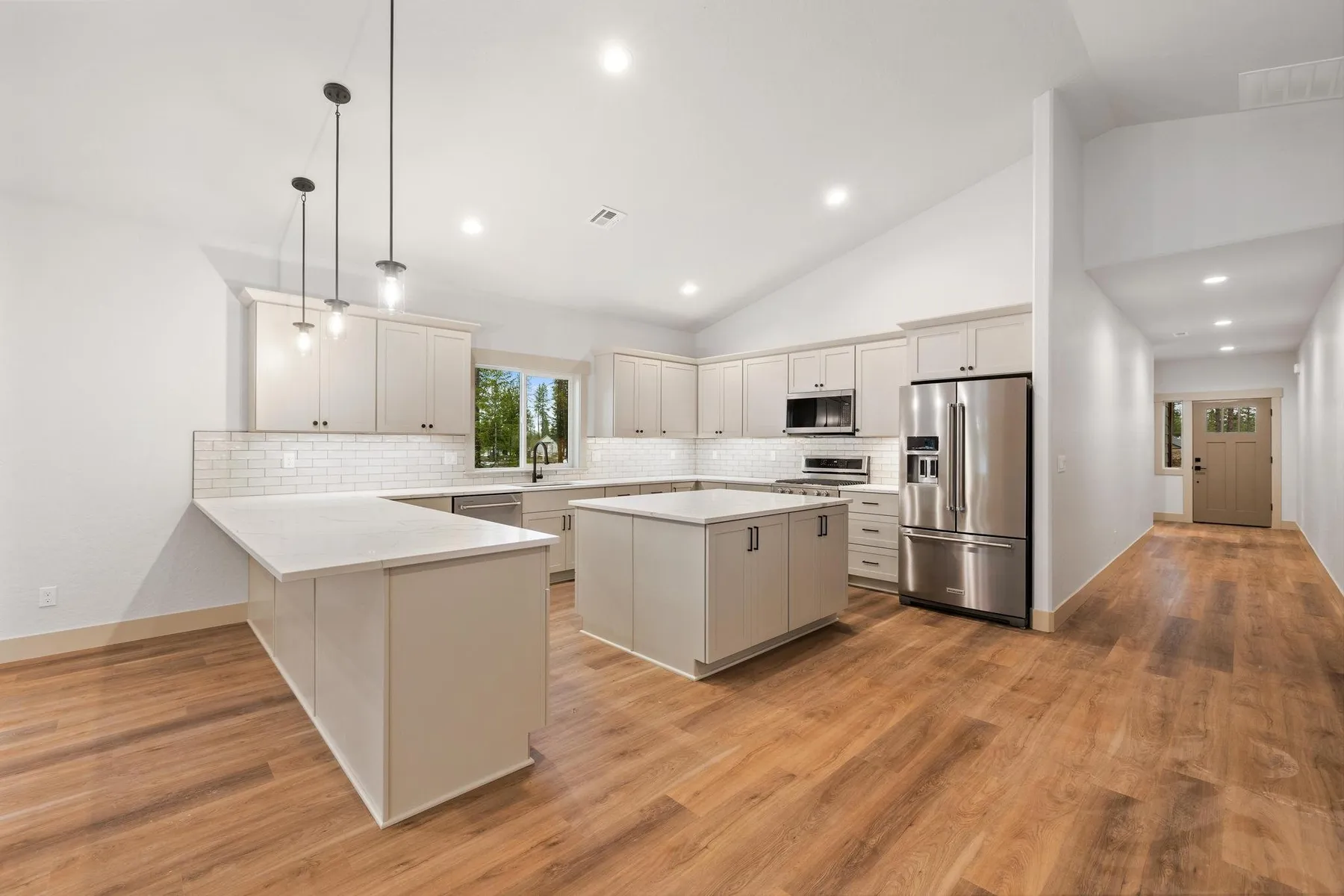 Kitchen with off-white cabinetry, a quartz peninsula and island, stainless appliances and pendant lights.