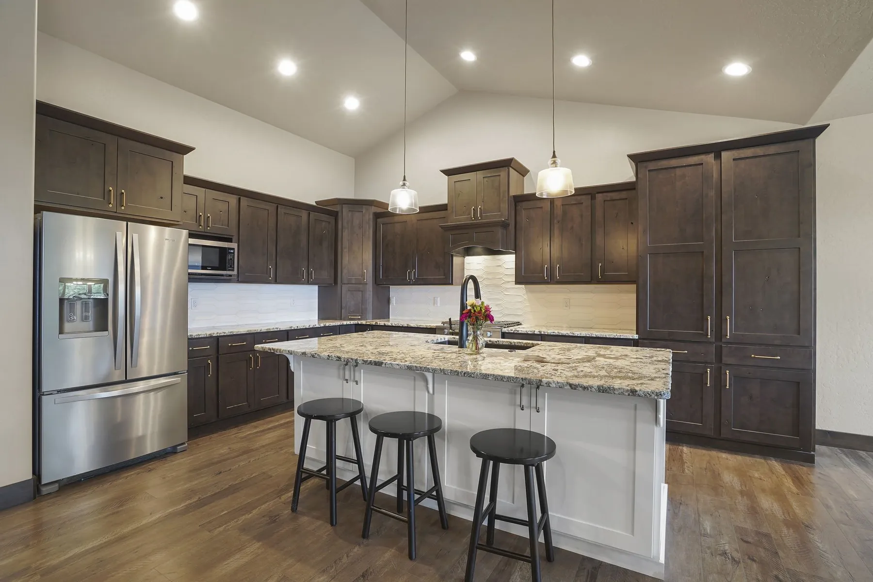 Kitchen with dark wood cabinets, stainless appliances and a white island with a granite top and three bar stools.