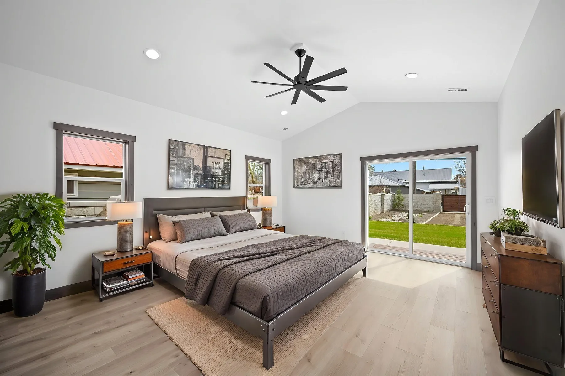 Main-floor primary bedroom with a sliding glass door to the backyard, a ceiling fan and framed art above the bed.