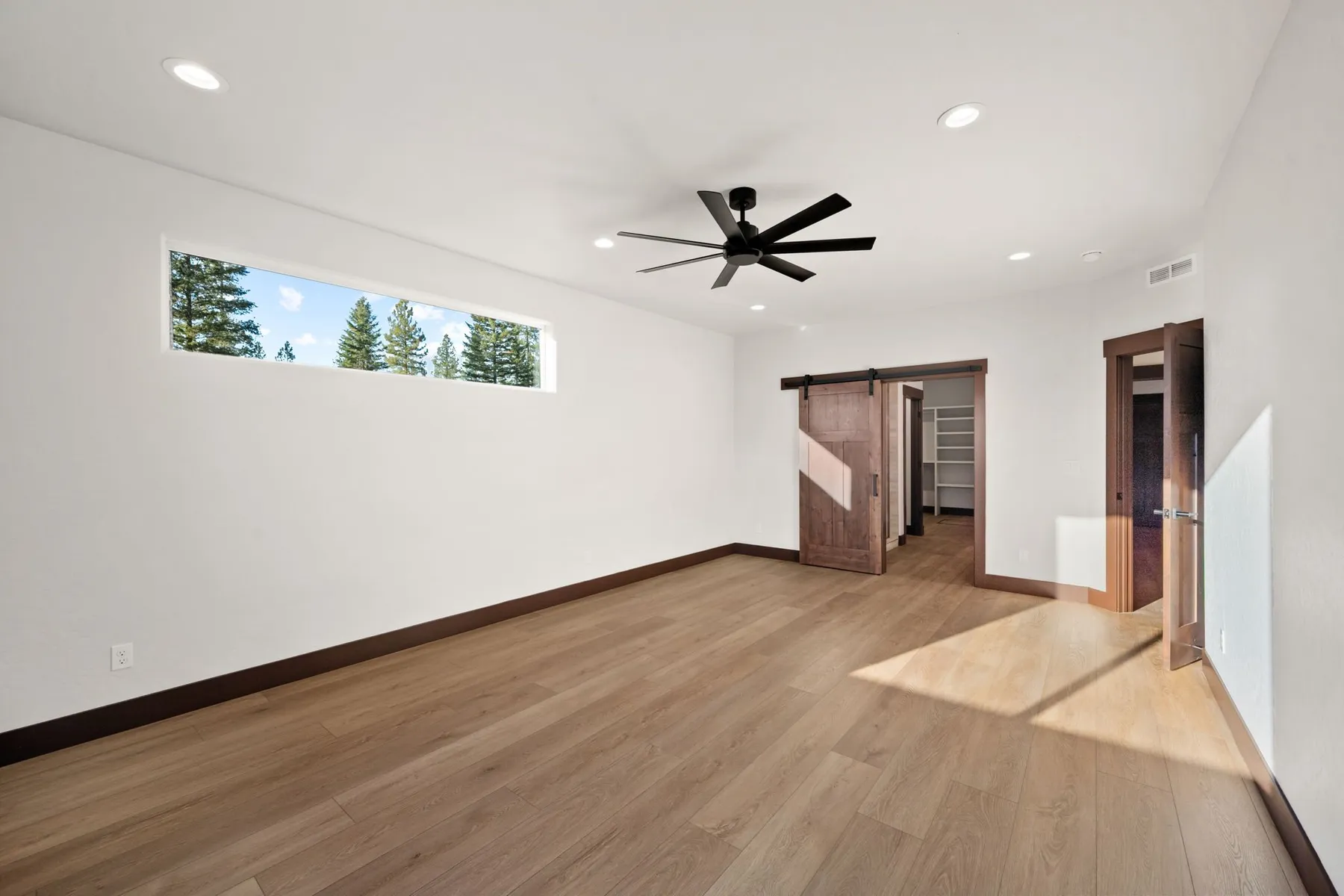 Primary bedroom with a ceiling fan, a long clerestory window and a sliding barn door leading to the walk-in closet.