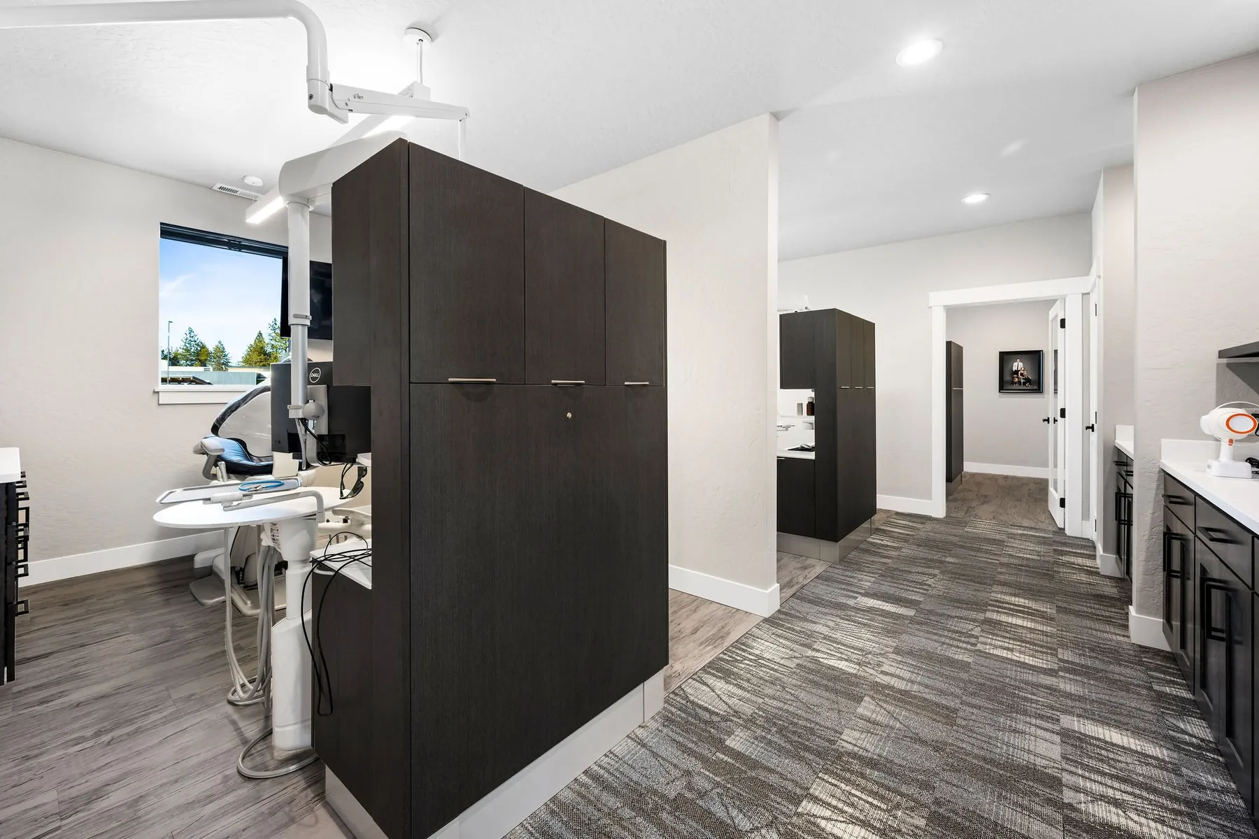 Hallway between open treatment bays separated by dark wood cabinet partitions.