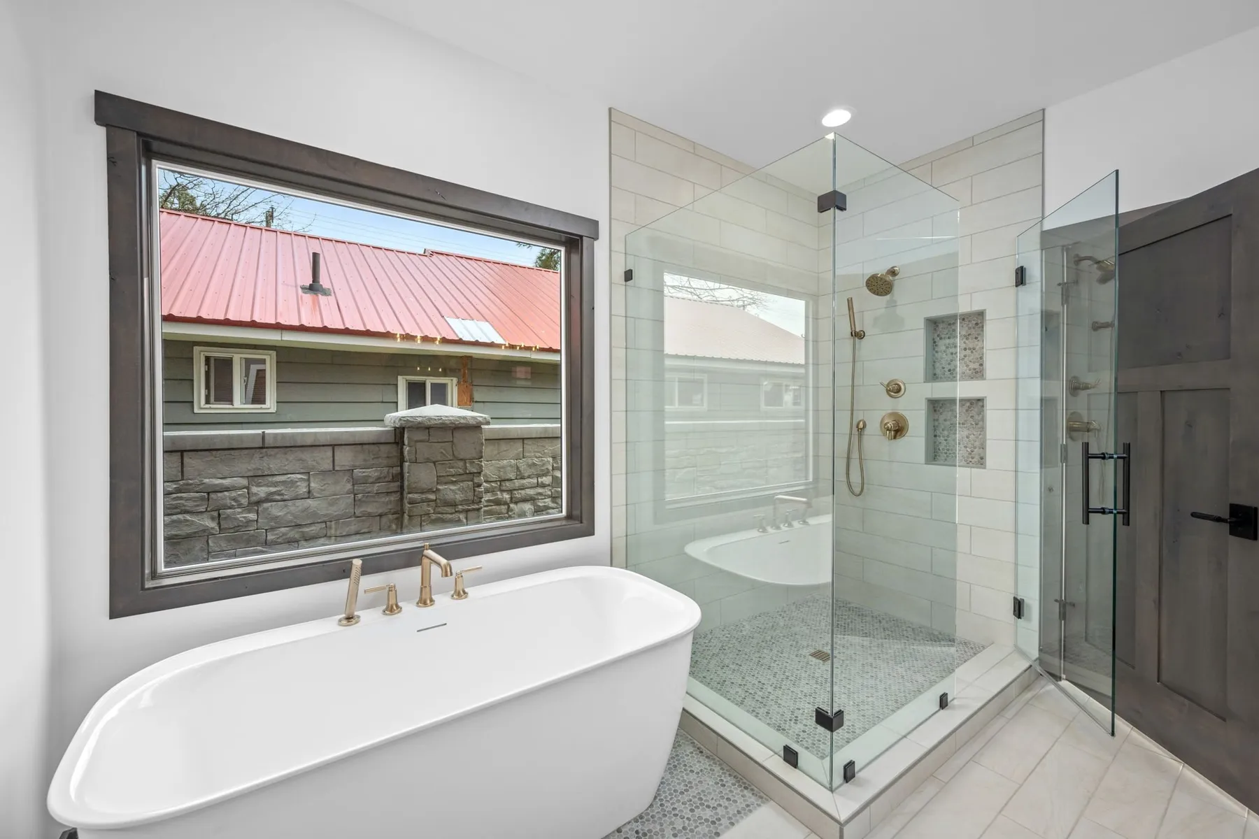 Primary bathroom with a freestanding soaking tub under a large window and a glass-enclosed tile shower with brass fixtures.