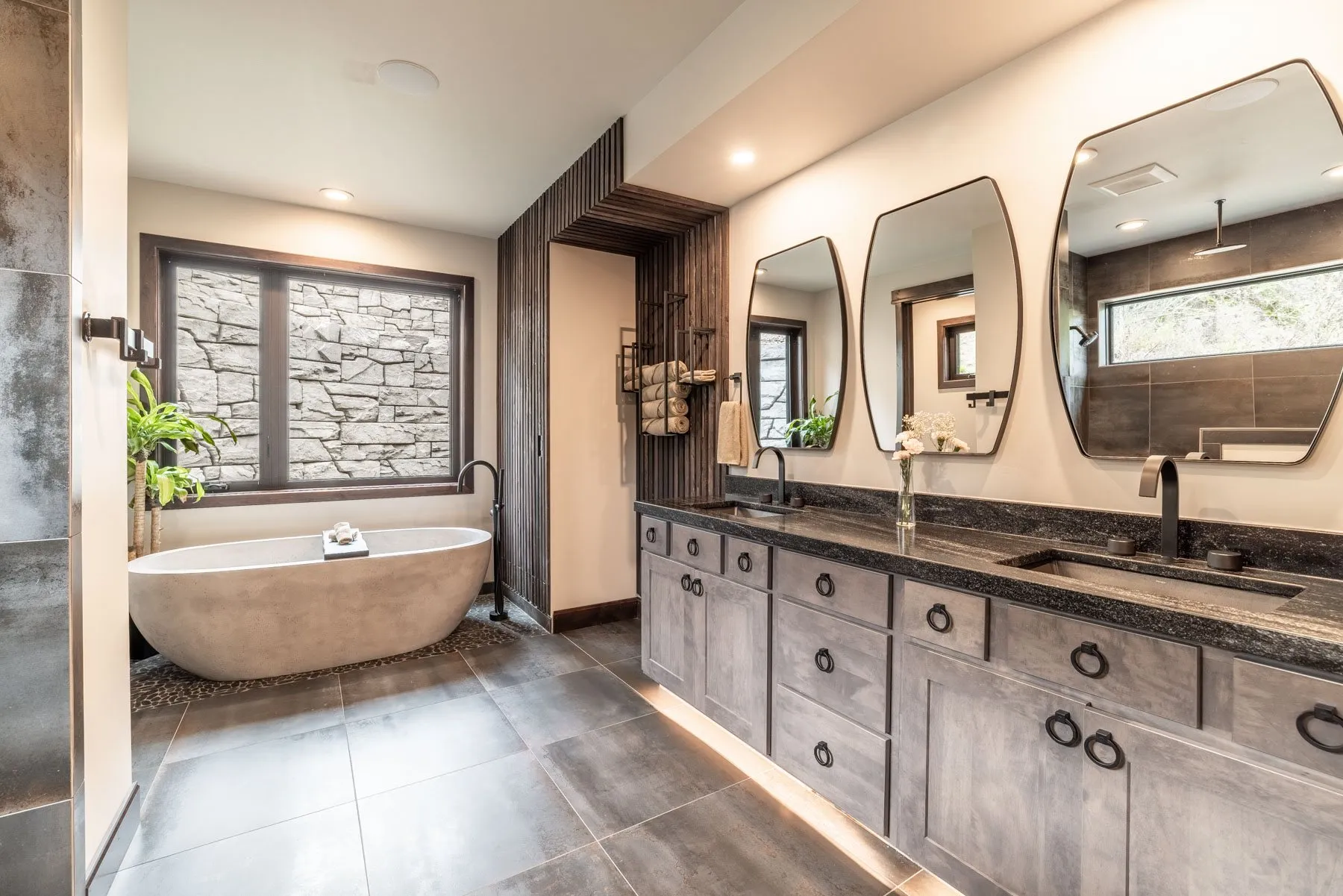 Primary bathroom with a freestanding stone tub, a long double vanity with three arched mirrors and a stone accent wall.