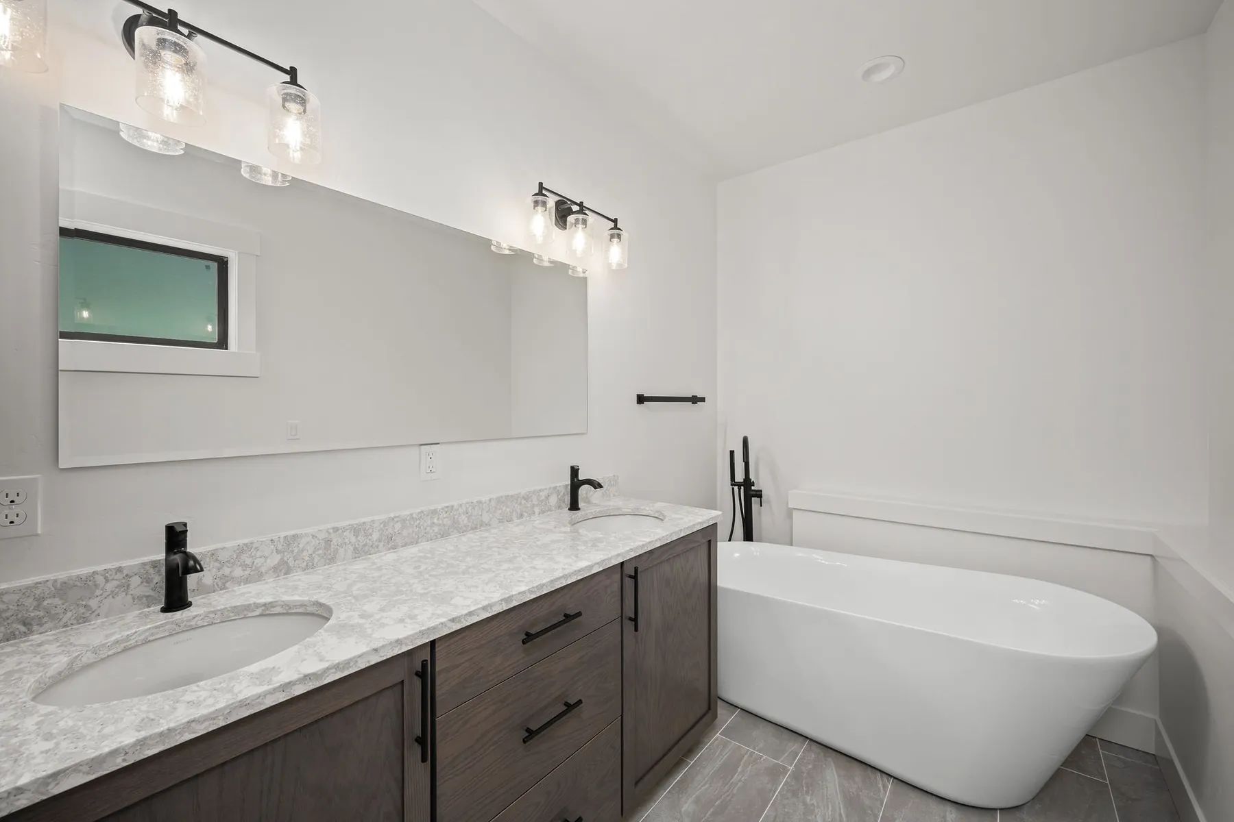 Bathroom with a dark wood double vanity, quartz countertop, black faucets and a freestanding tub.