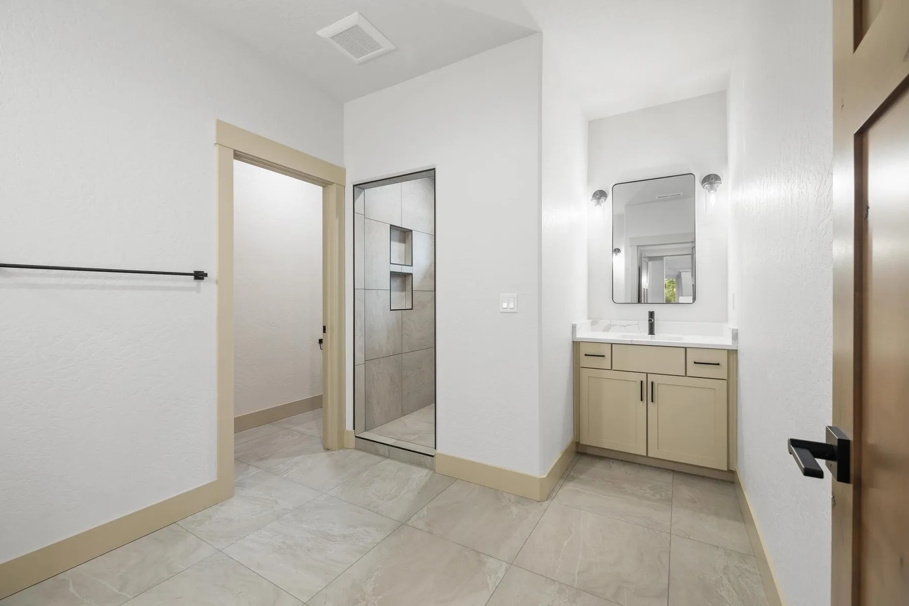 Primary bathroom with a tiled walk-in shower, a light wood vanity and the walk-in closet through a side doorway.