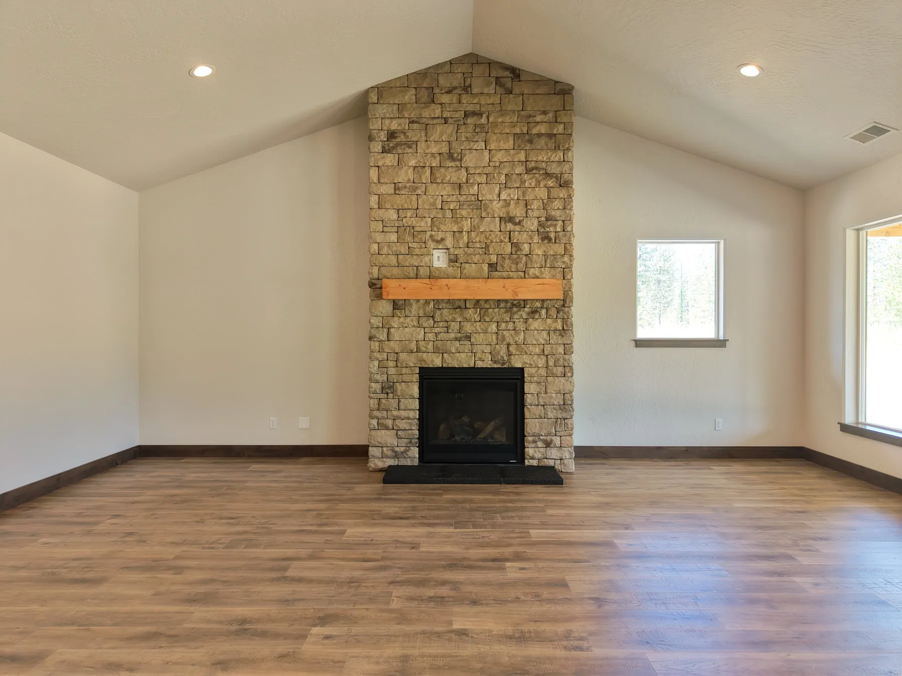 Vaulted living room with a floor-to-ceiling stone fireplace, a wood mantel and LVP flooring.