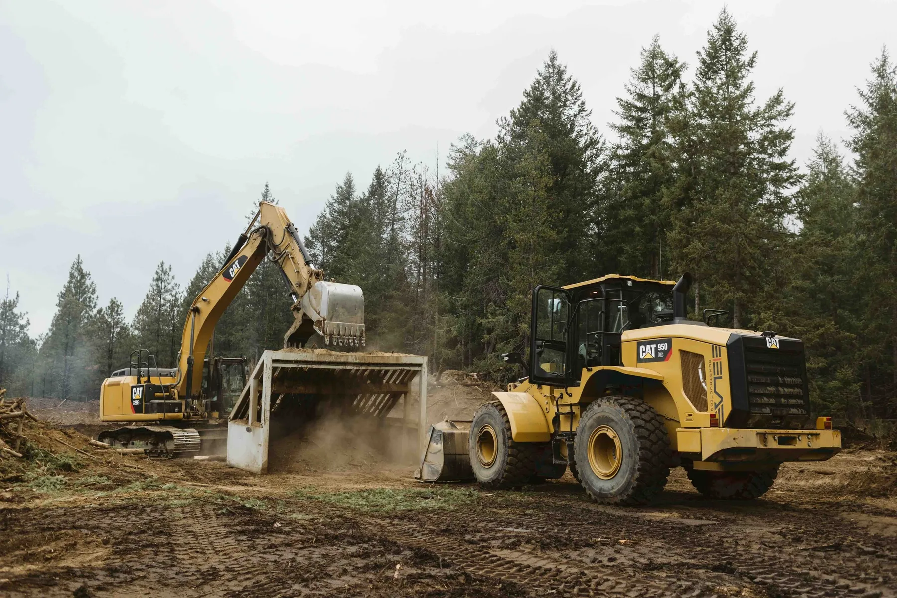 Excavator loading debris into a screening plant while a CAT wheel loader works beside it on the cleared site.