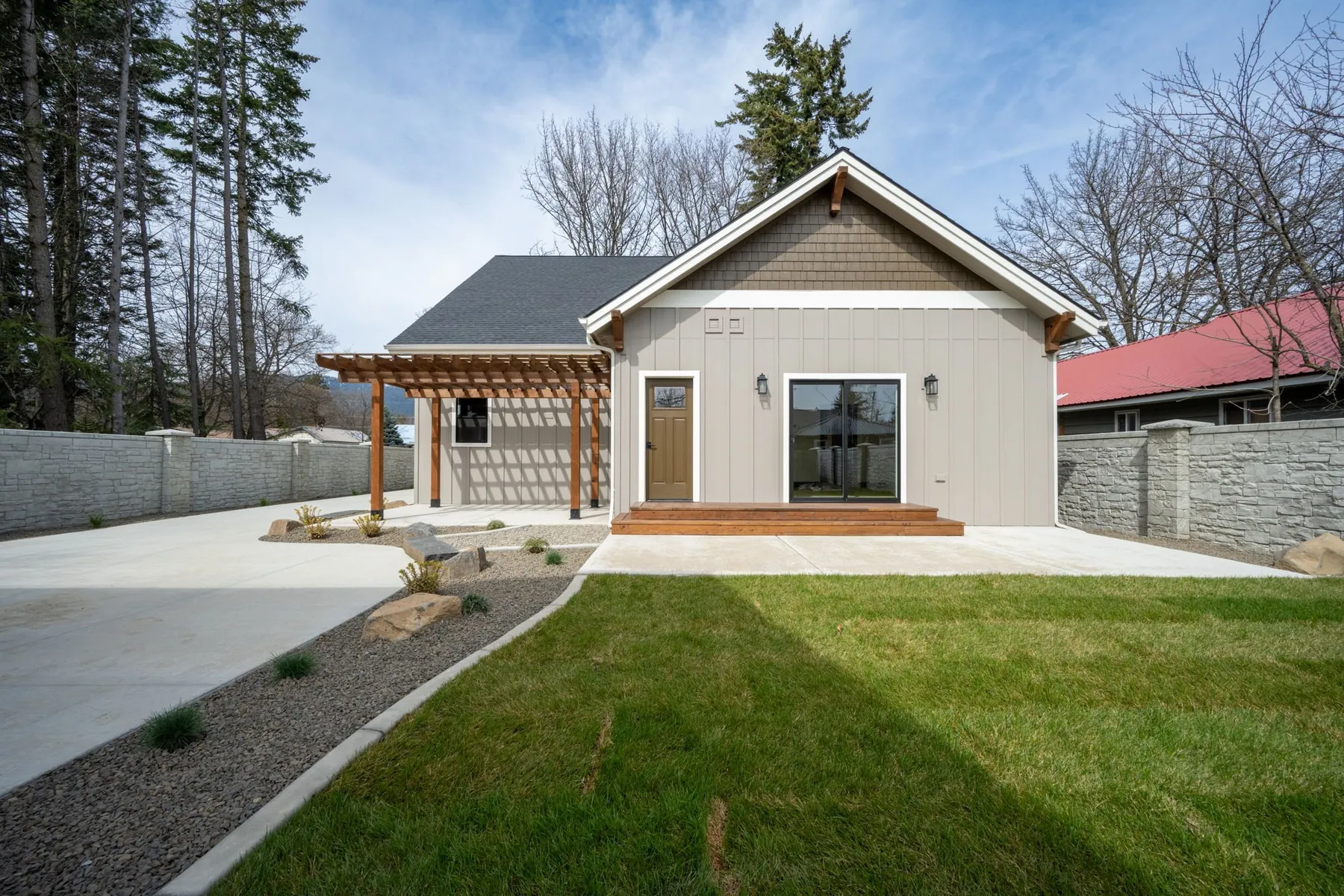 Backyard of the property with a timber pergola beside the shop and ADU, a concrete patio and a stone-block privacy wall.