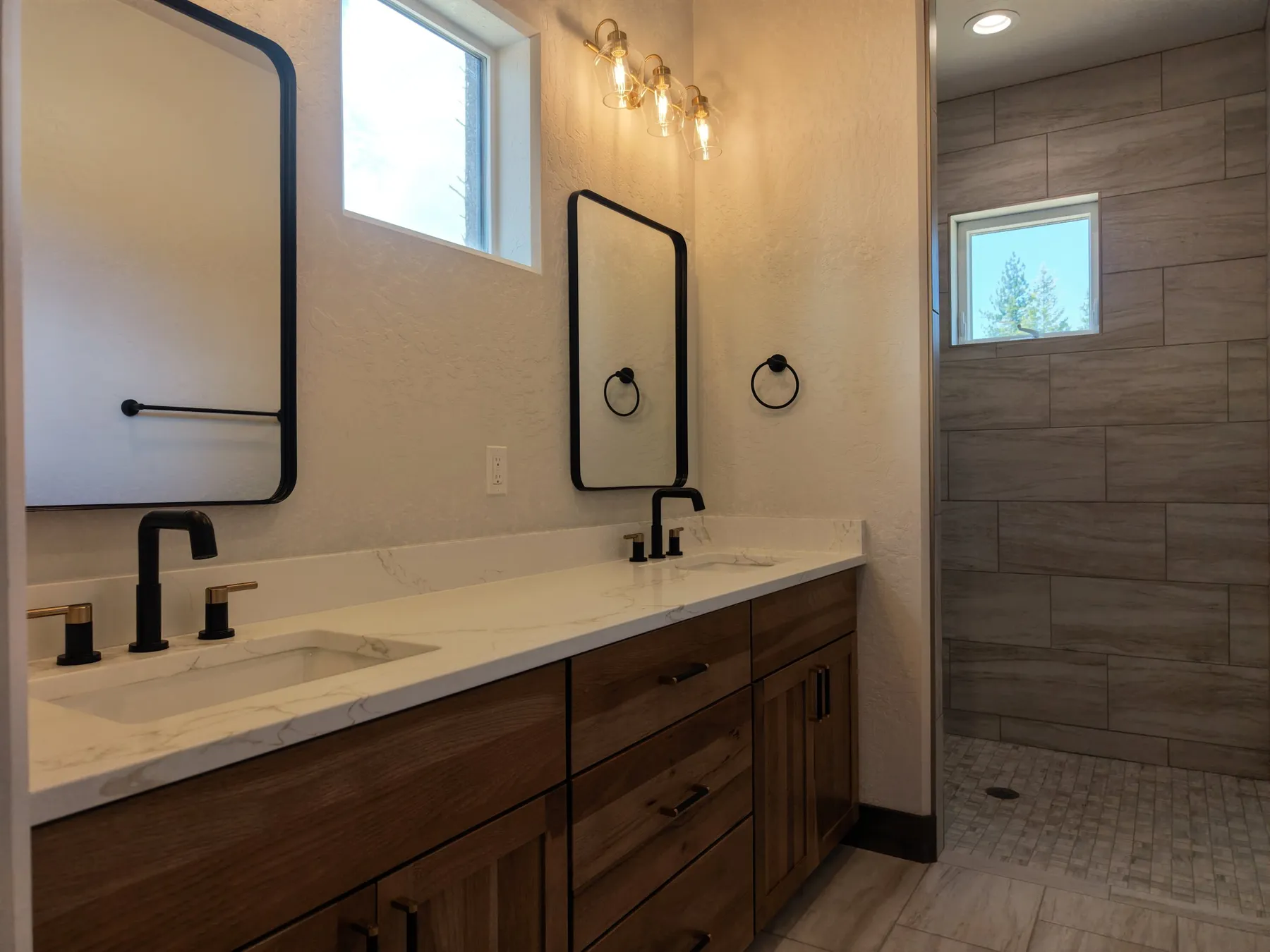 Bathroom with a hickory double vanity, white quartz top, black faucets and a wood-look tile walk-in shower.