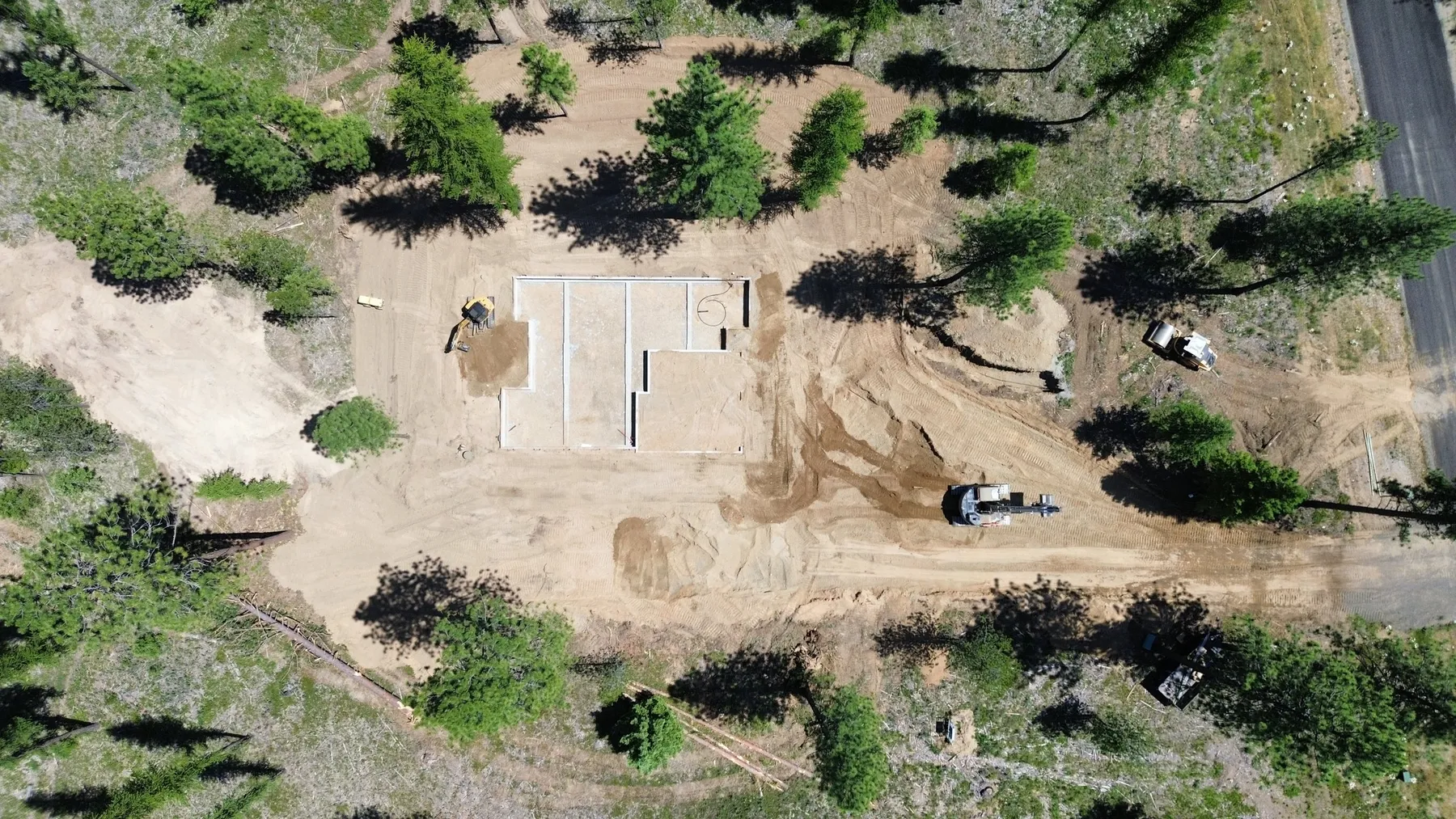 Aerial view of the Radiant homesite during construction, with a new foundation and excavated ground among the pines.
