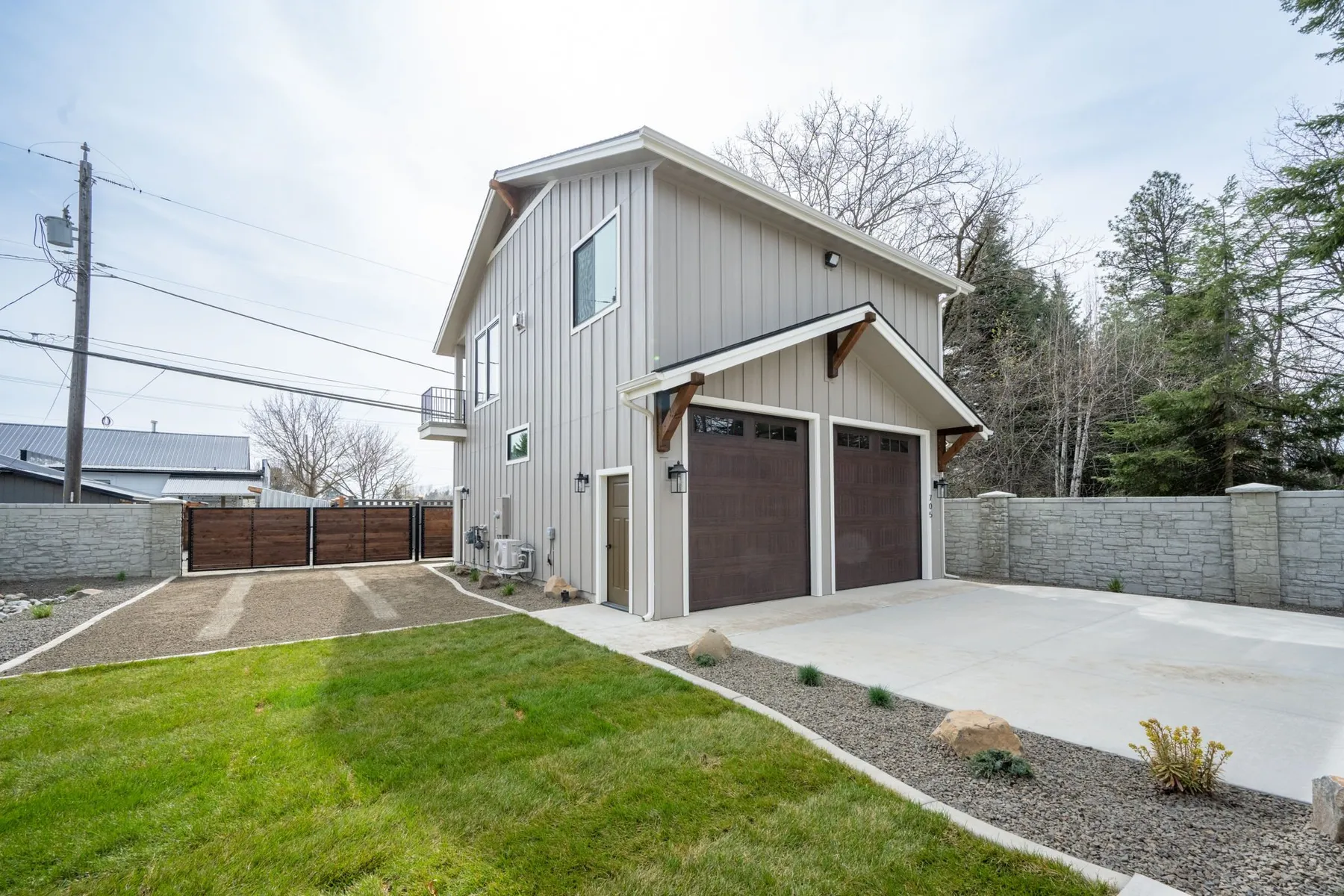 Two-story shop with a two-car garage and the ADU above, enclosed by a stone-block wall and a wood driveway gate.
