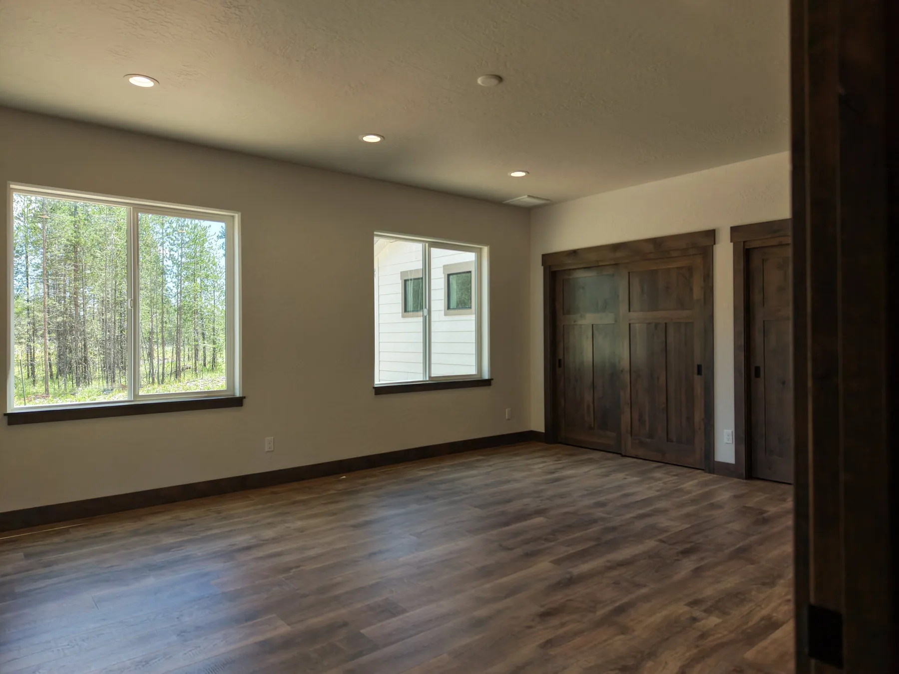 Bedroom with dark plank flooring, two windows facing the pines and wide double closet doors.