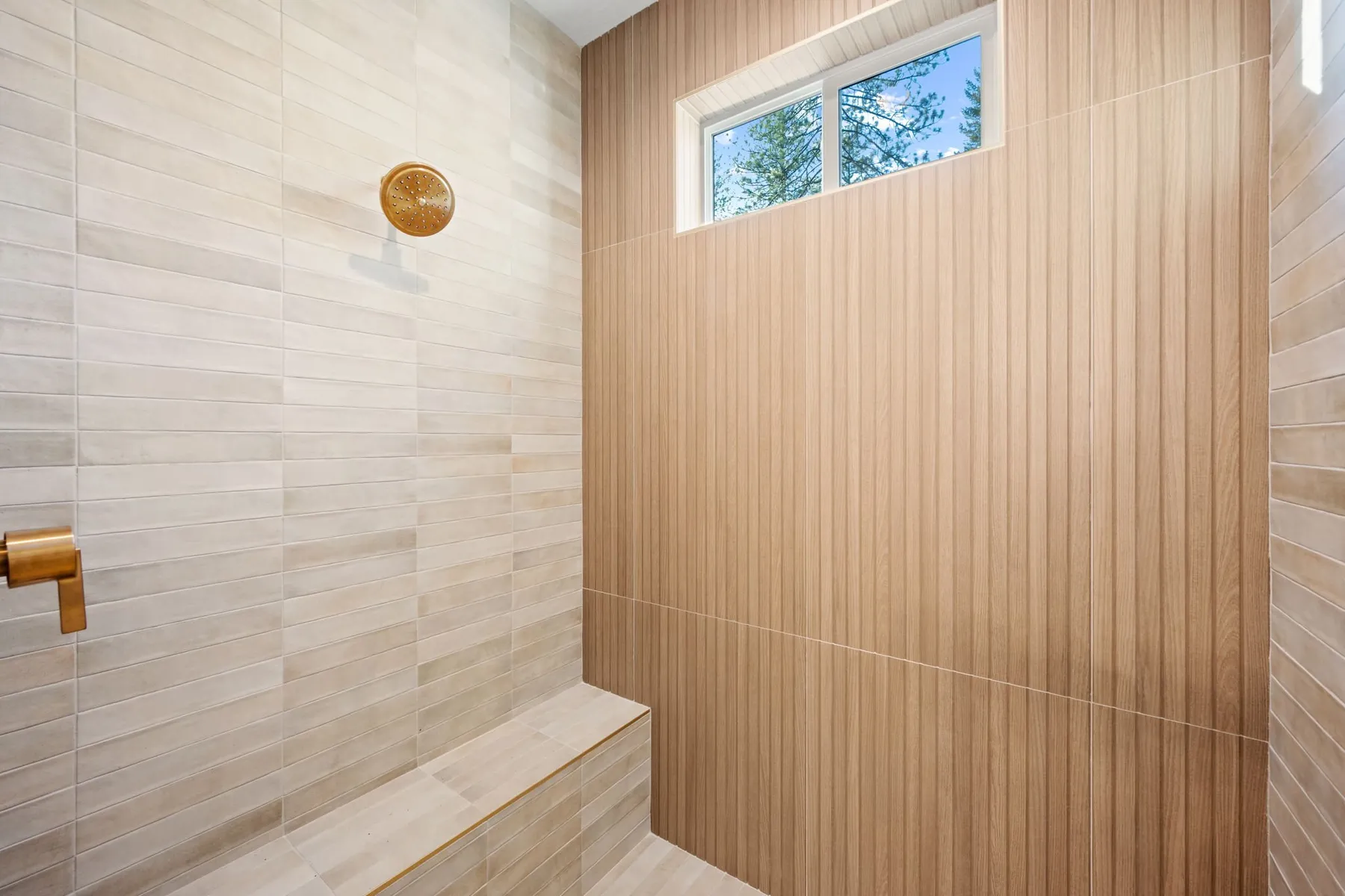 Walk-in tile shower with wood-look tile walls, a gold rain shower head and a built-in bench under a small window.