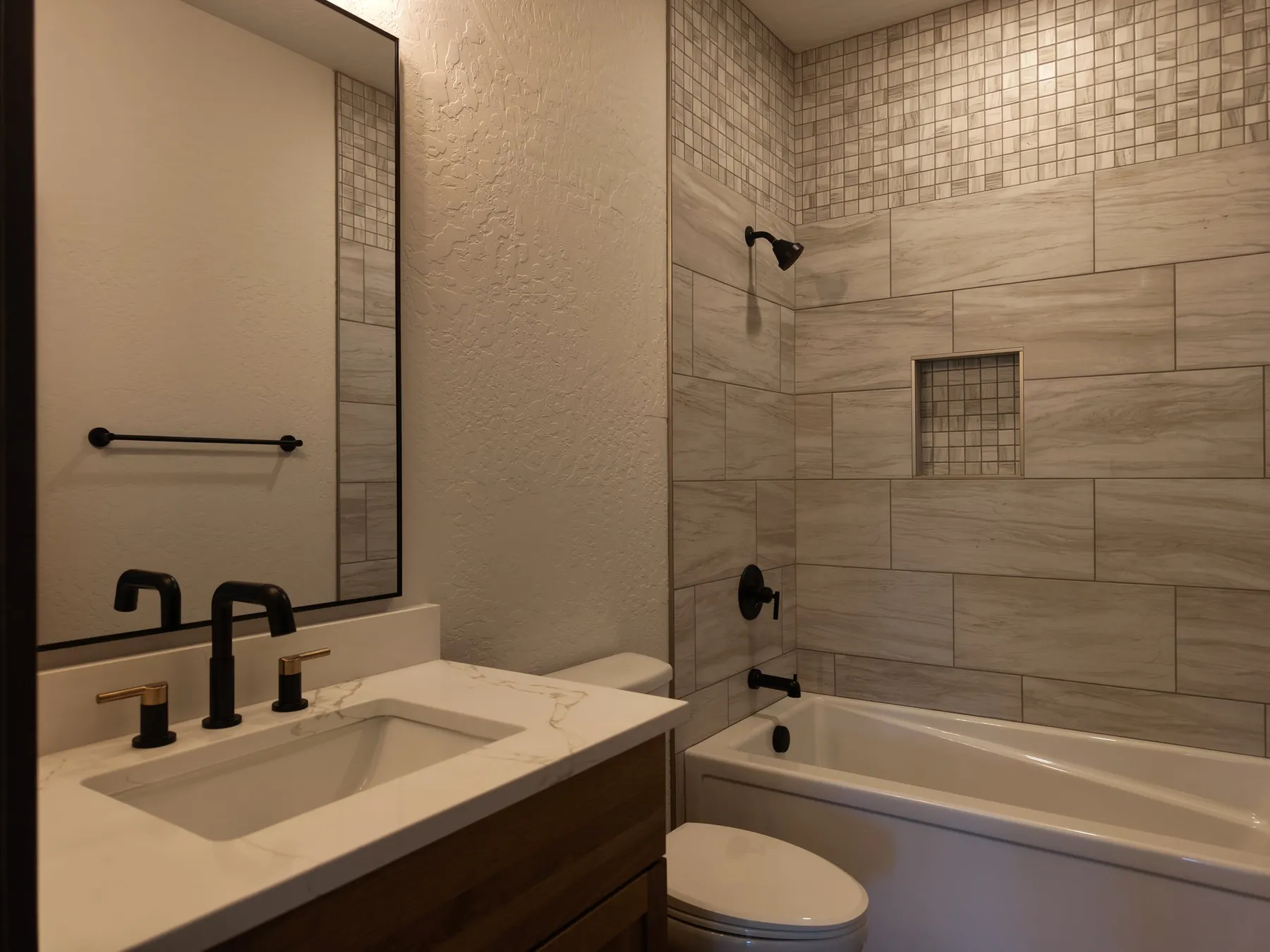Guest bathroom with a tub and shower in wood-look tile with a mosaic niche, and a quartz vanity with black fixtures.