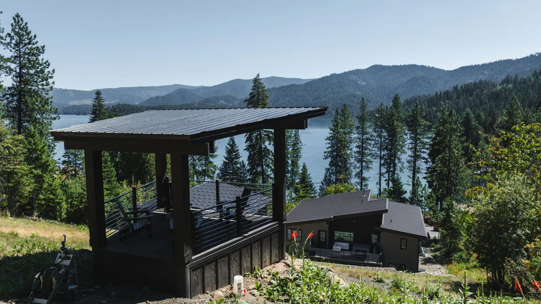 Hillside gazebo with a dark metal roof overlooking the home and Hayden Lake, with forested mountains beyond.