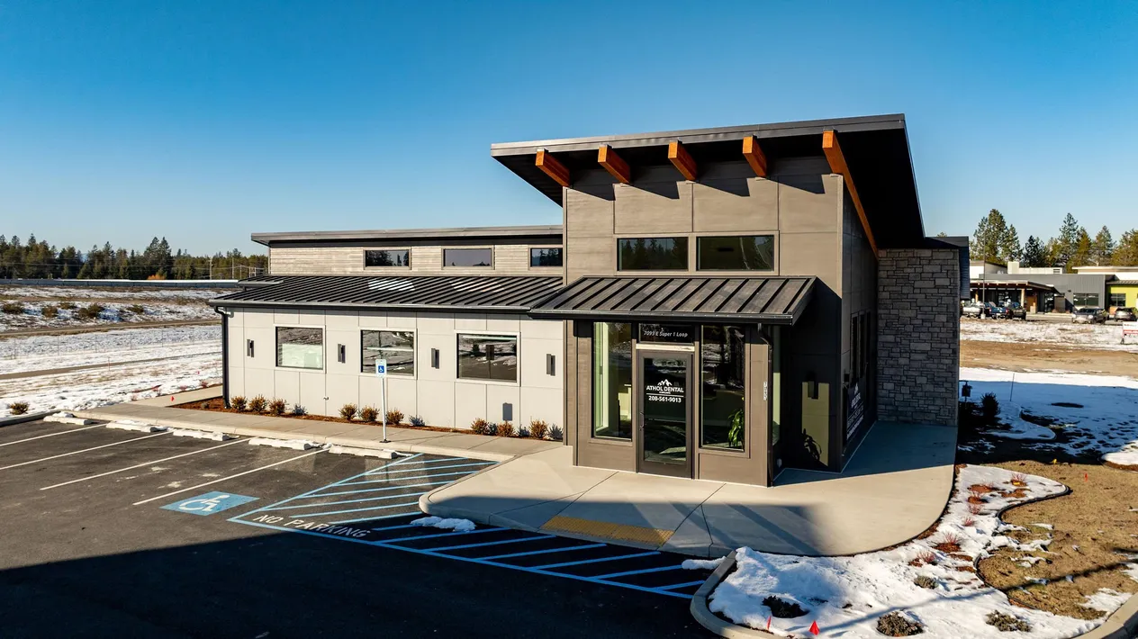 Exterior of the Athol Dental office, a single-story commercial building with a raised shed roof, exposed wood beams, stone accents and a new parking lot in winter.