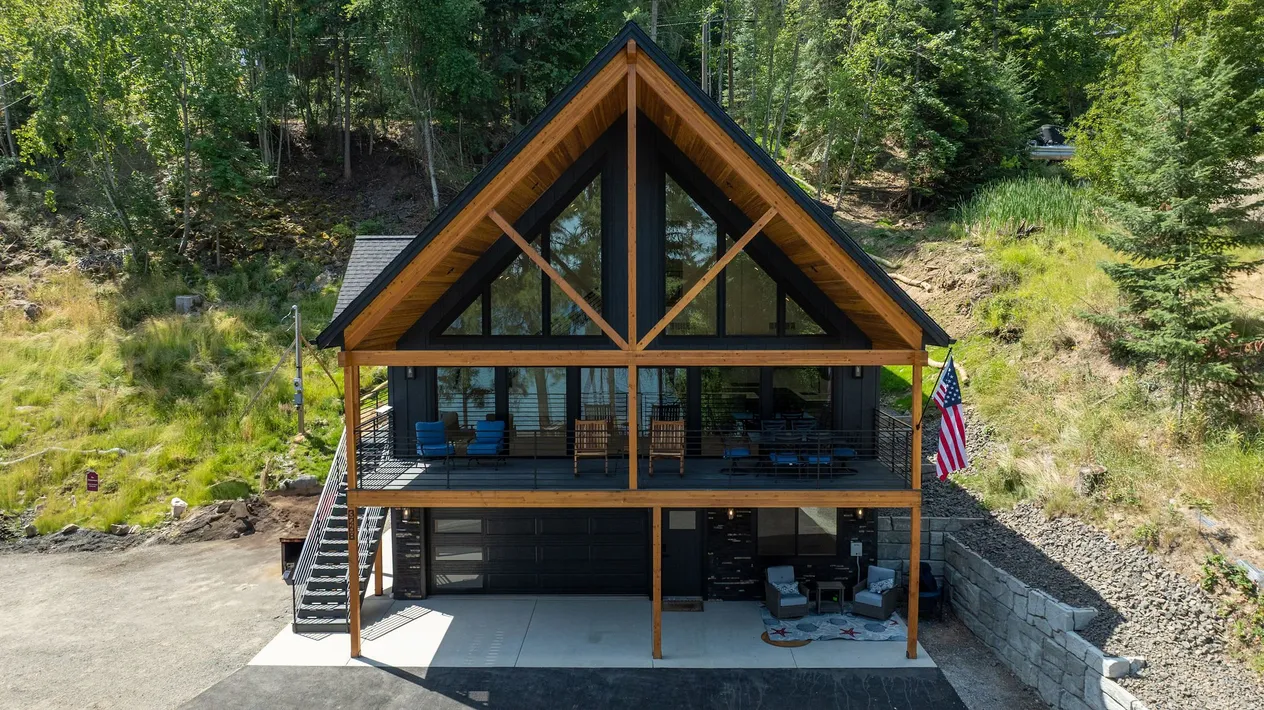 Aerial view of The Overlook, a lake house with a towering A-frame glass gable, cedar-stained exposed beams and a full-width deck on a hillside.