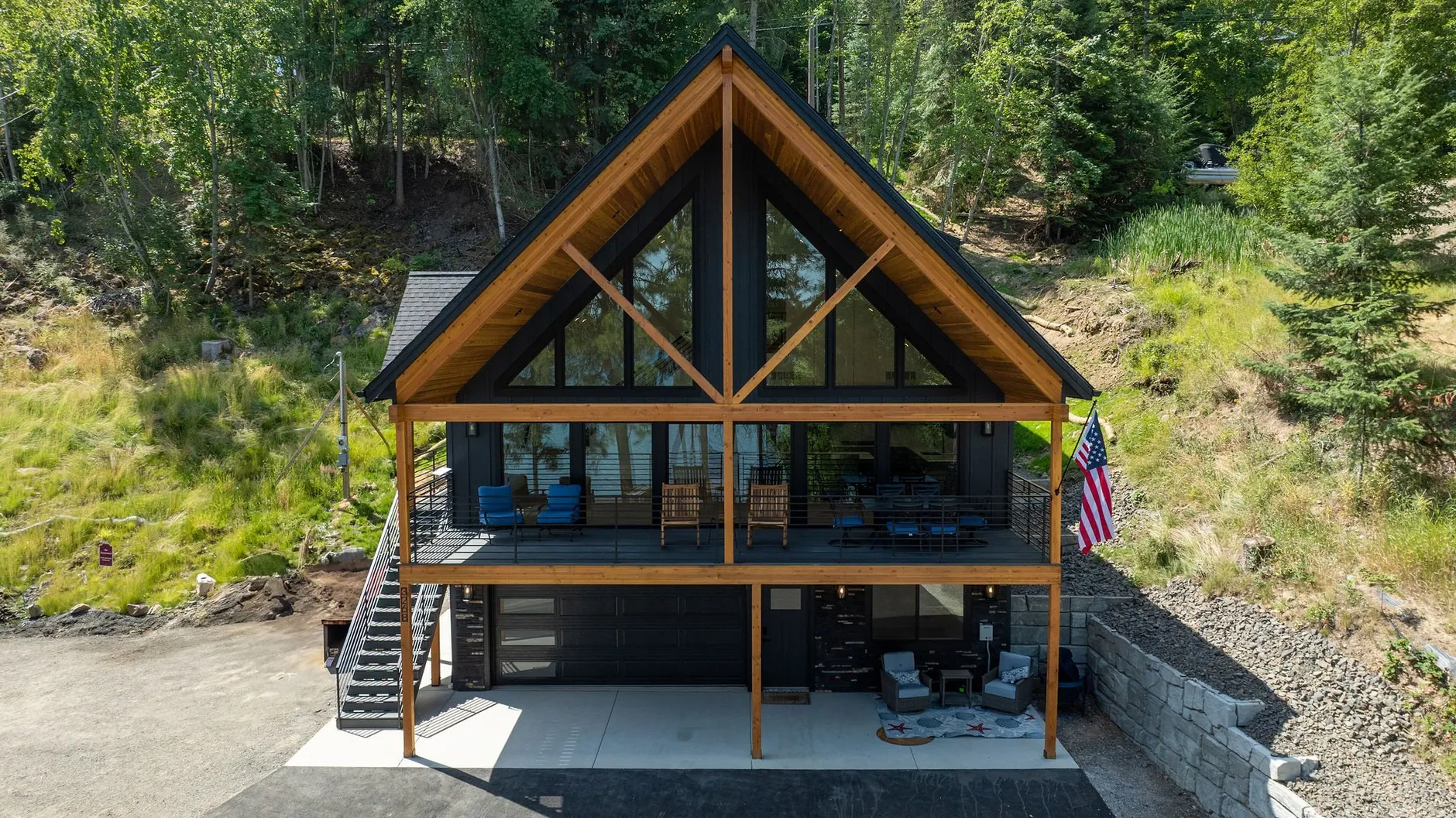 Aerial view of The Overlook, a lake house with a towering A-frame glass gable, cedar-stained exposed beams and a full-width deck on a hillside.