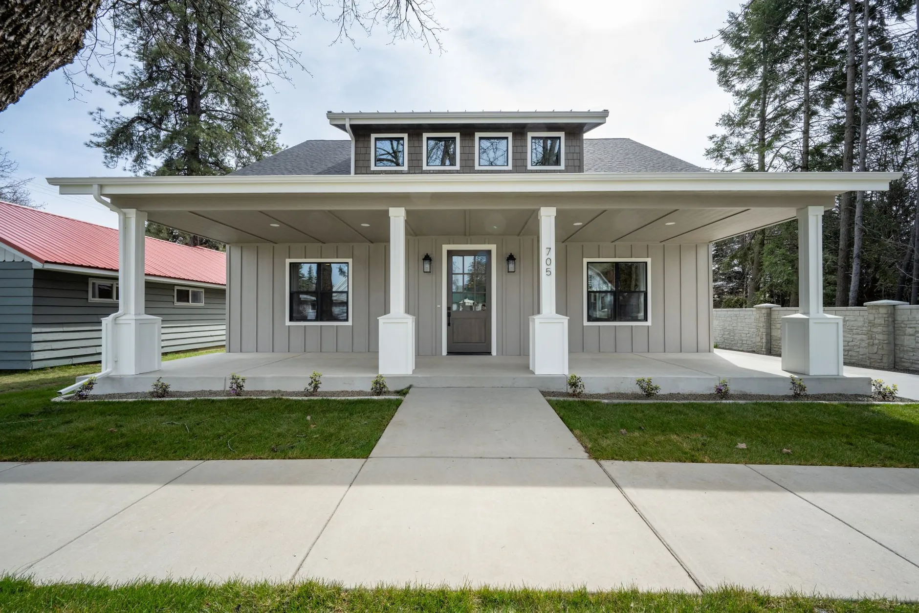 Craftsman-style home with a full-width covered front porch on white tapered columns, gray board-and-batten siding and a dormer above, behind a new lawn.