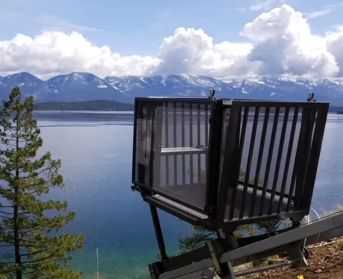 A Marine Innovations tram car on a steep hillside track above a lake, with snow-capped mountains across the water.